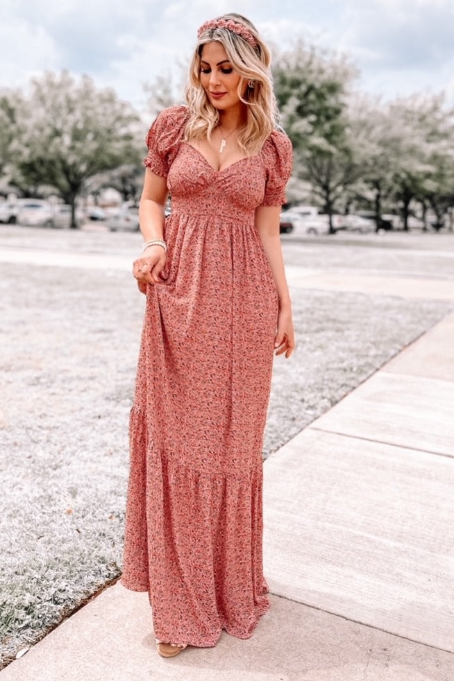 woman wearing a pink floral maxi dress with puff sleeves and a tiered skirt, standing outdoors