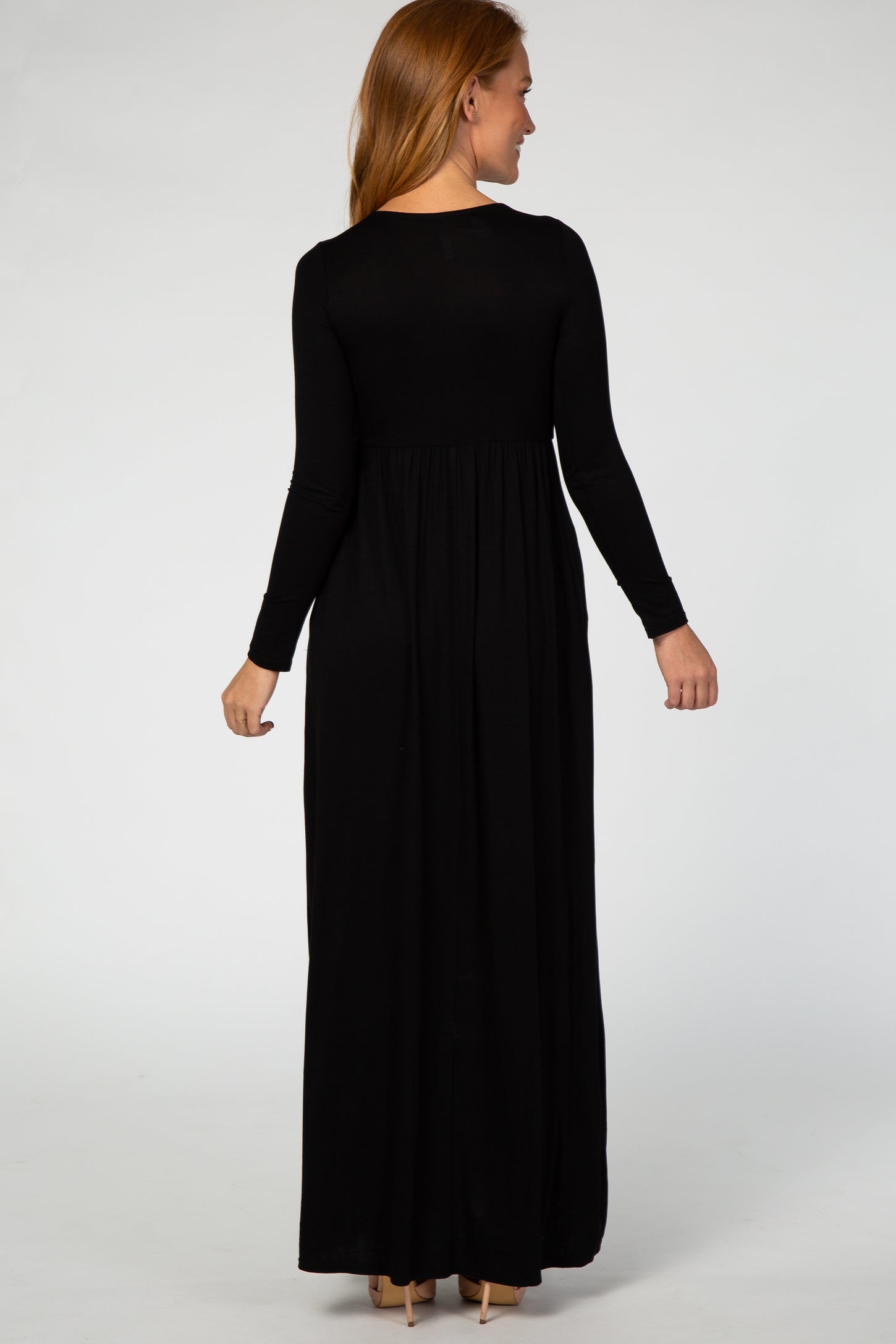 woman wearing a black long sleeve maxi dress, viewed from the back, with a fitted bodice and flowing skirt