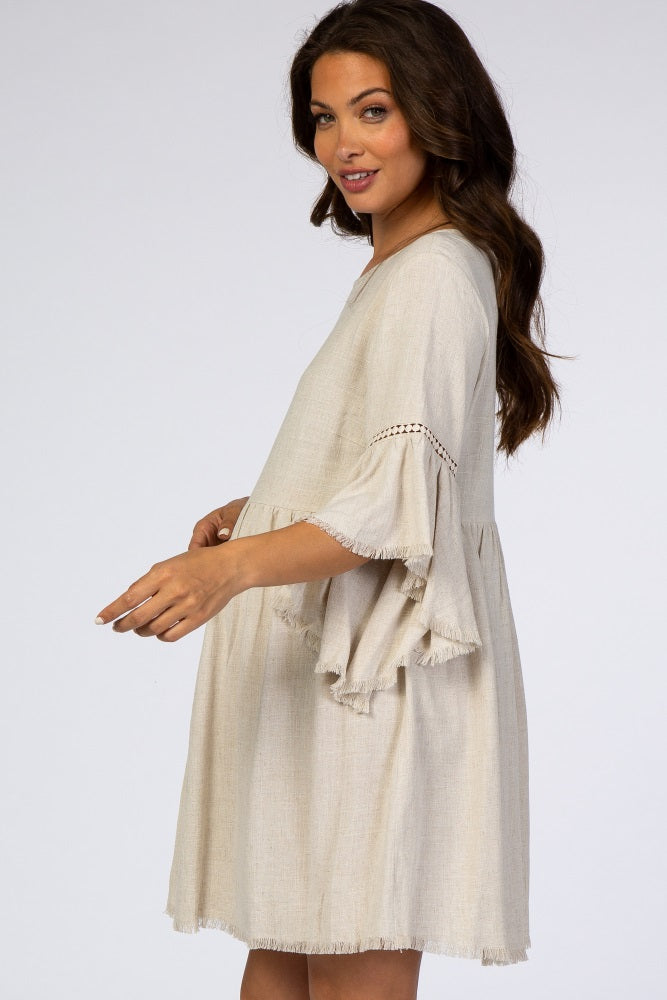woman wearing a beige maternity dress with flared sleeves and fringe detail, showing a baby bump