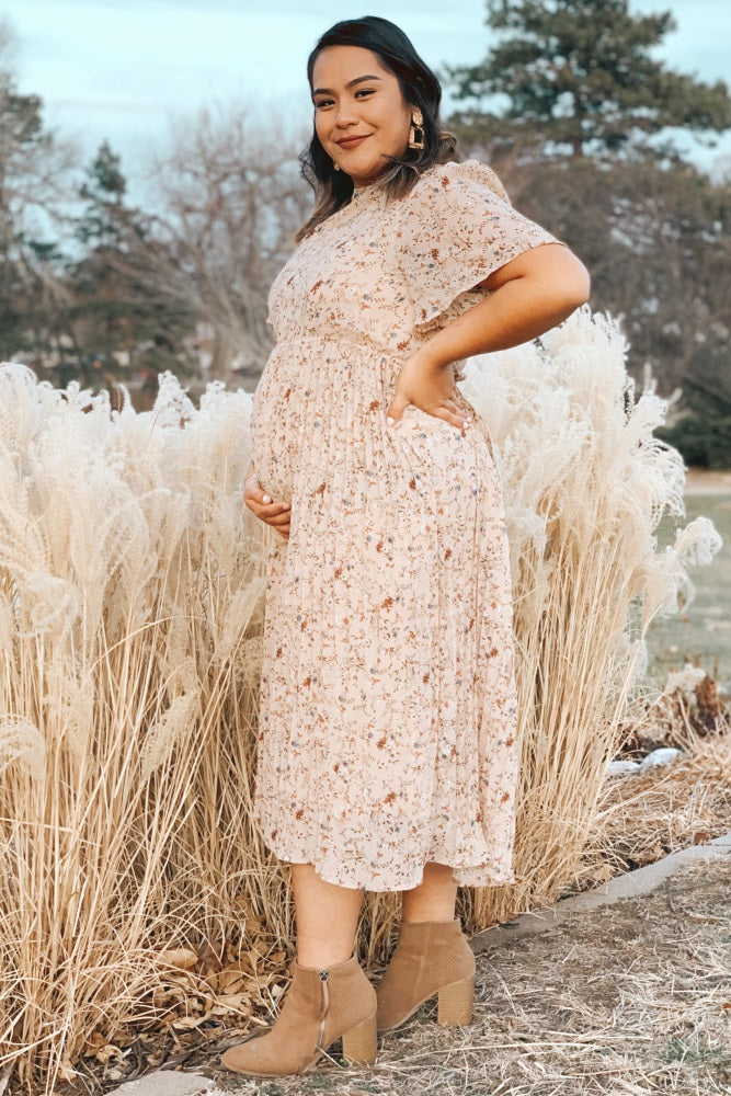 pregnant woman in floral midi dress and tan ankle boots posing in front of tall pampas grass