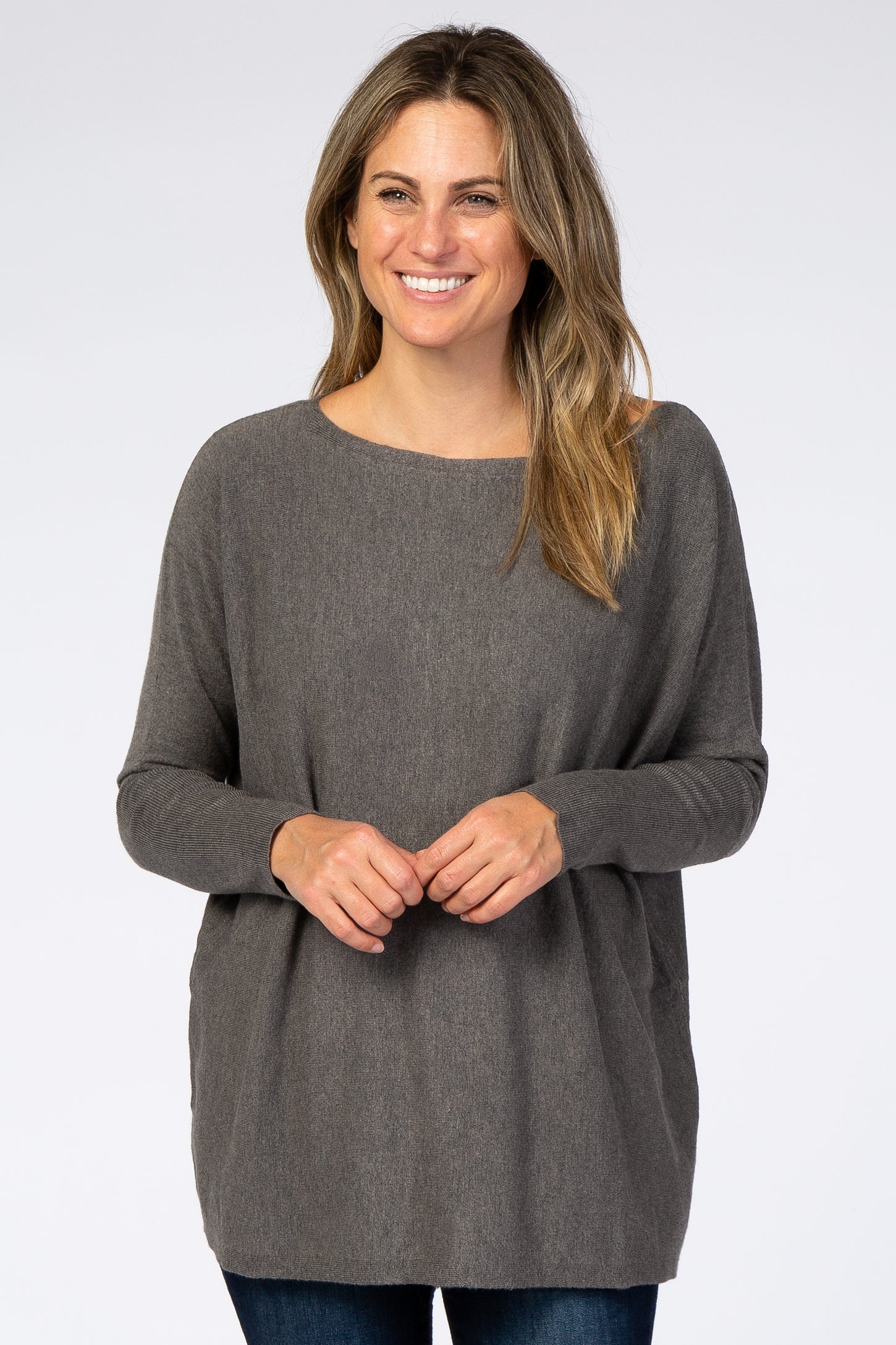 woman wearing a dark gray oversized sweater with a wide neckline and long sleeves, smiling at the camera