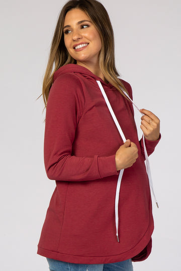 woman wearing a burgundy maternity hoodie with a scalloped hem and a white drawstring, showcasing her baby bump