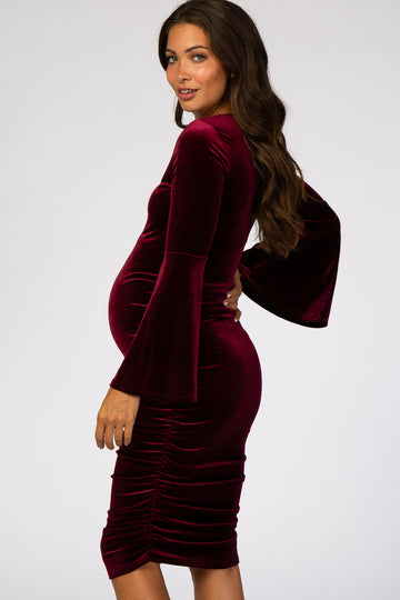 woman wearing a burgundy velvet maternity dress with bell sleeves and ruching, showing her baby bump