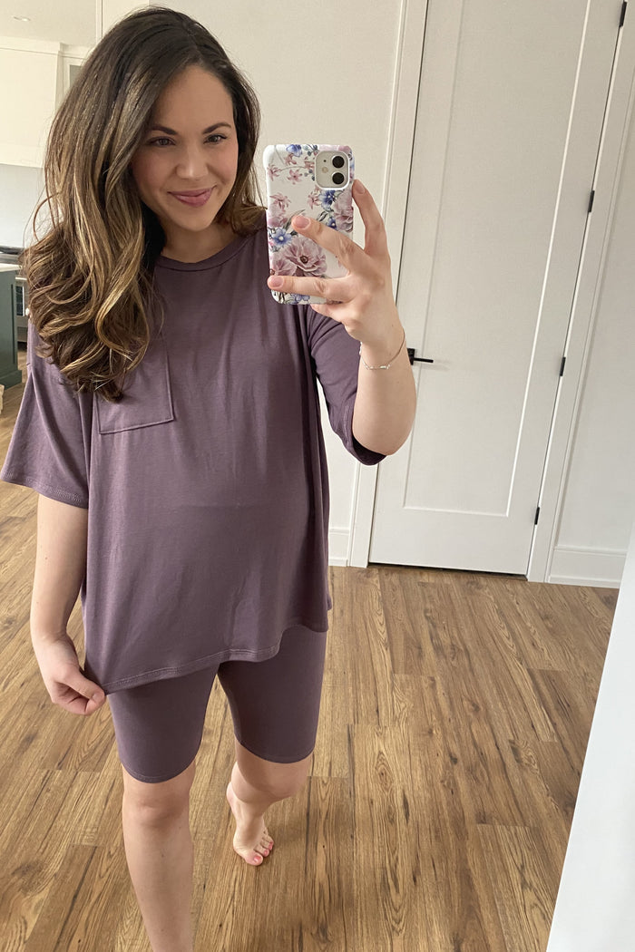 woman wearing a mauve maternity t-shirt with a pocket and matching bike shorts, showing baby bump while taking a selfie