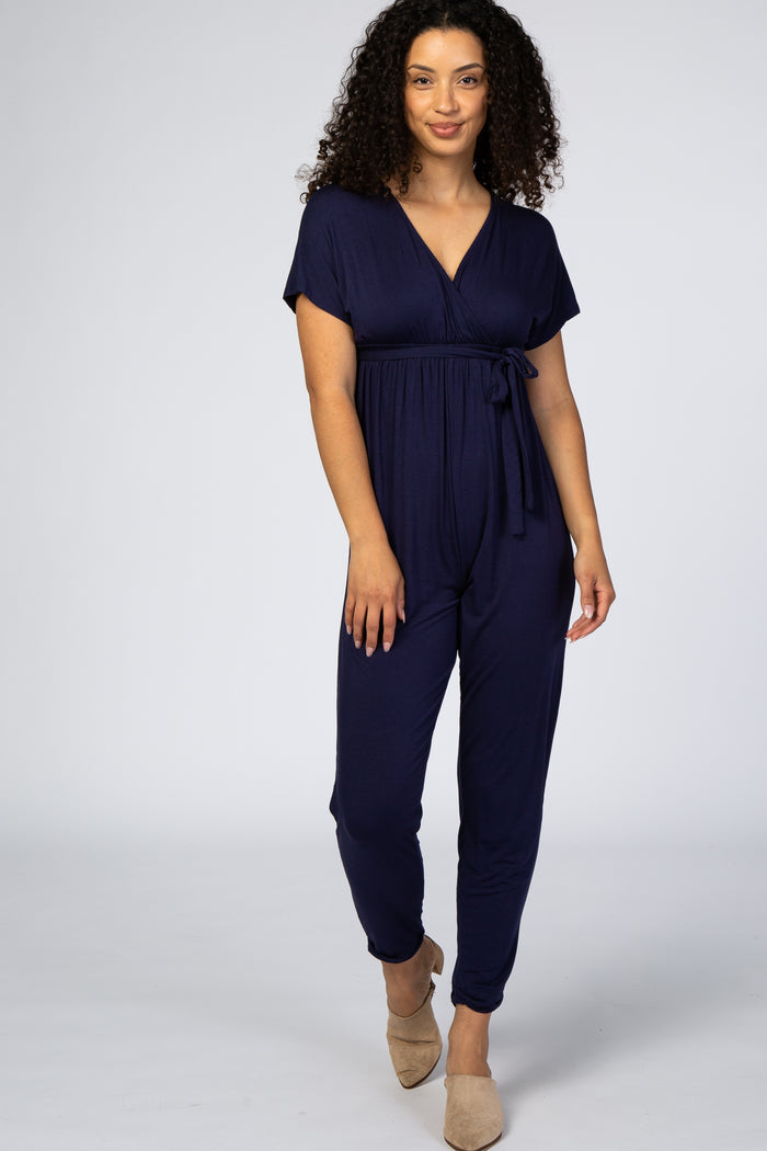 woman wearing a navy blue short sleeve jumpsuit with a wrap front and tie waist detail