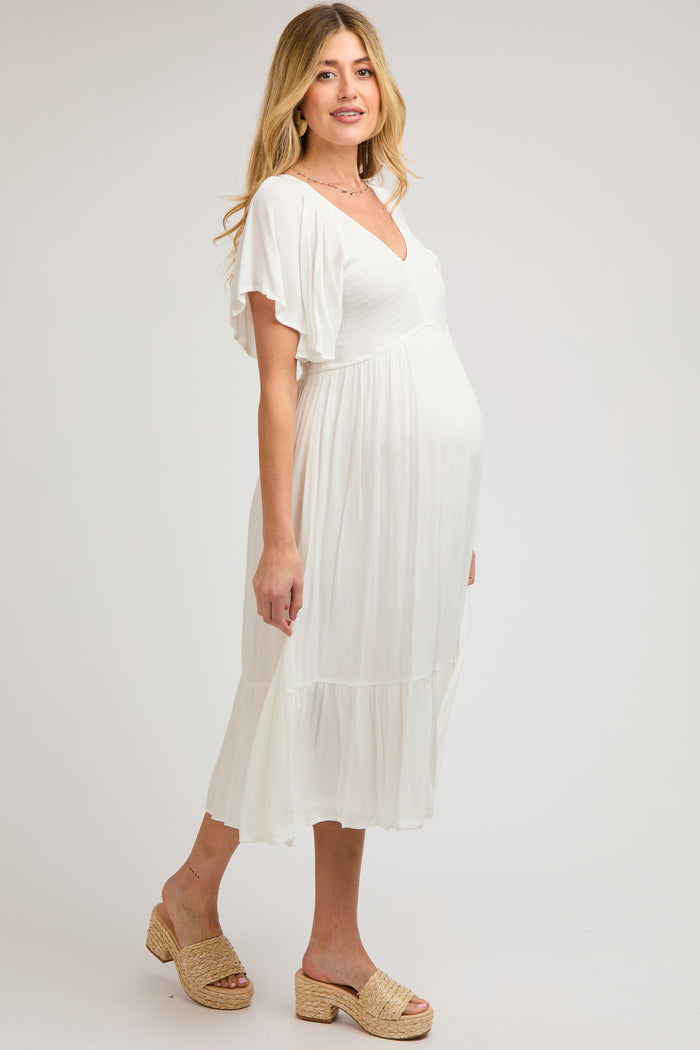 woman wearing a white maternity dress with flutter sleeves and a flowing skirt, highlighting her baby bump