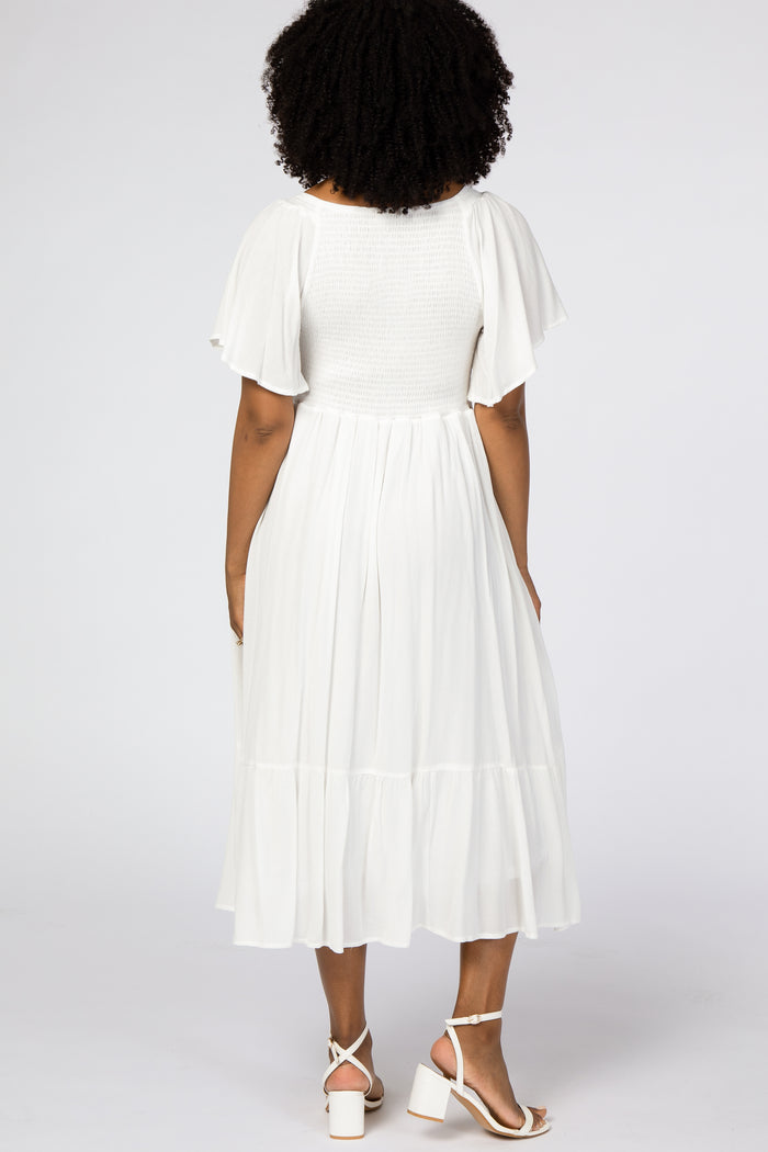 woman wearing a white midi dress with short flutter sleeves and a tiered skirt, showing the back view