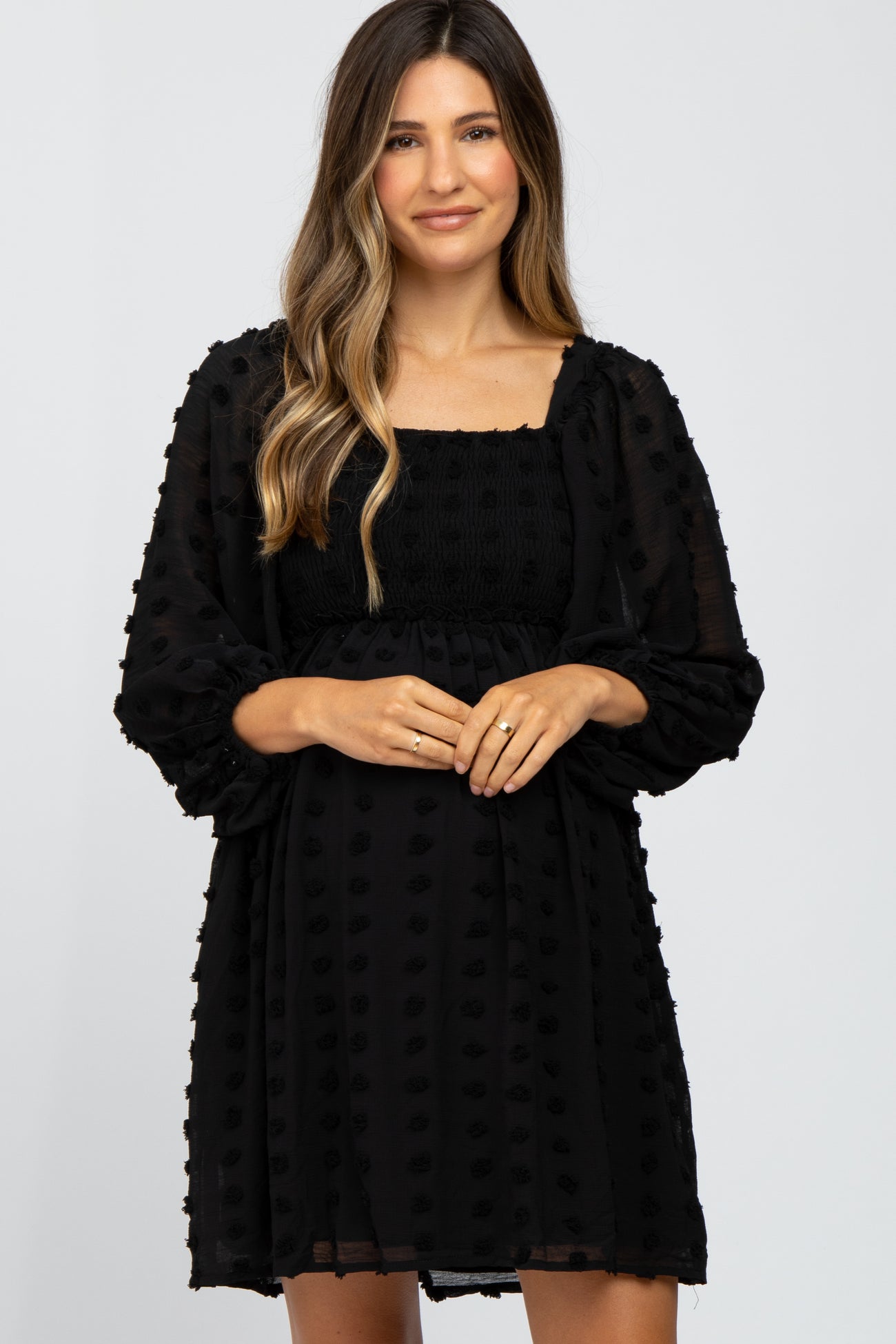 woman wearing a black maternity dress with a square neckline and puff sleeves, highlighting her baby bump