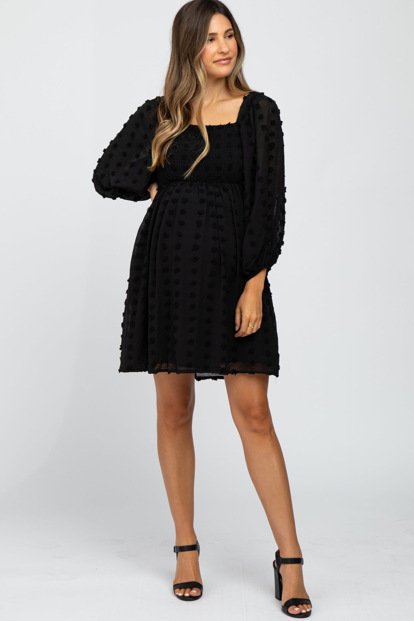 woman wearing a black maternity dress with puff sleeves and a textured dot pattern, showing her baby bump