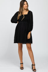 woman wearing a black maternity dress with puff sleeves and a textured dot pattern, showing her baby bump