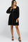 woman wearing a black maternity dress with puff sleeves and a textured dot pattern, showing her baby bump