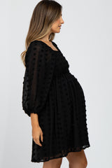 woman wearing a black maternity dress with textured dots and puff sleeves, showing her baby bump