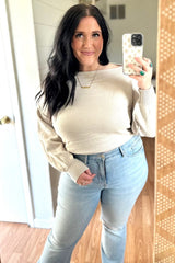 woman wearing a beige off-the-shoulder sweater and light blue distressed jeans, taking a mirror selfie