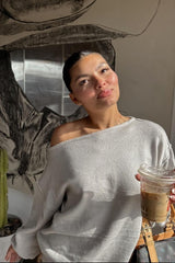 woman wearing a light grey off-the-shoulder sweater and holding a iced coffee drink