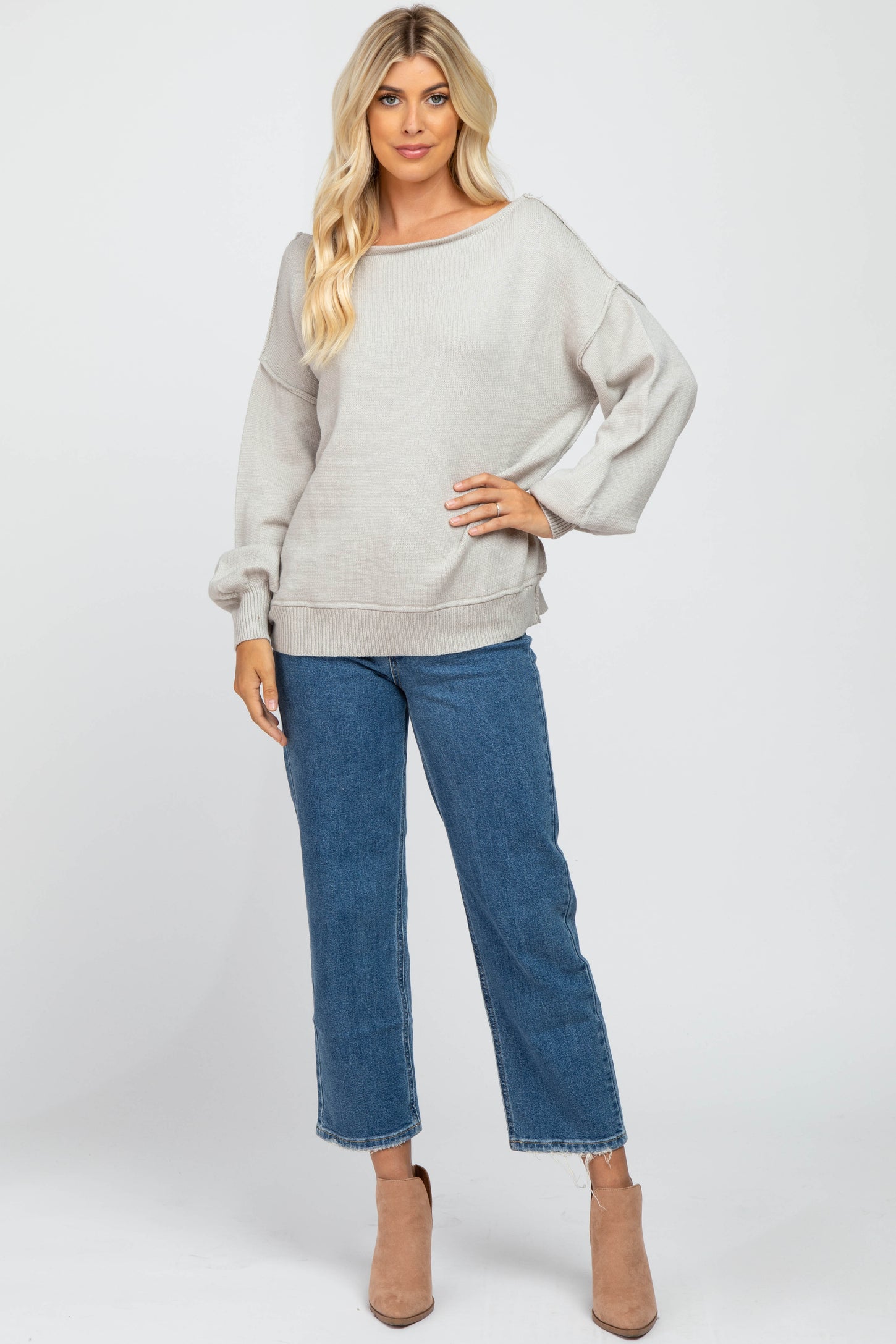 woman wearing a light grey oversized sweater with a wide neckline, paired with blue cropped jeans and beige ankle boots