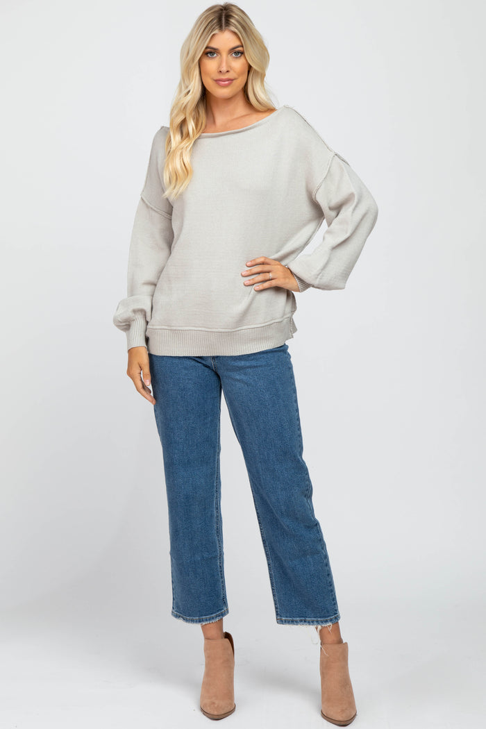 woman wearing a light grey oversized sweater with a wide neckline, paired with blue cropped jeans and beige ankle boots