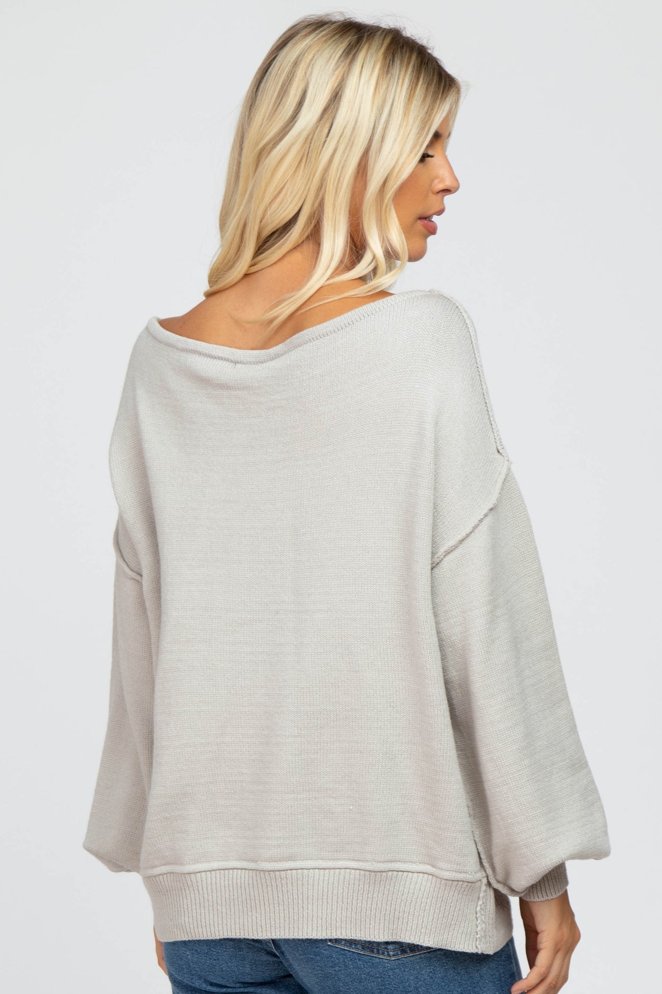 woman wearing a light gray oversized sweater with a wide neck and balloon sleeves, view from the back