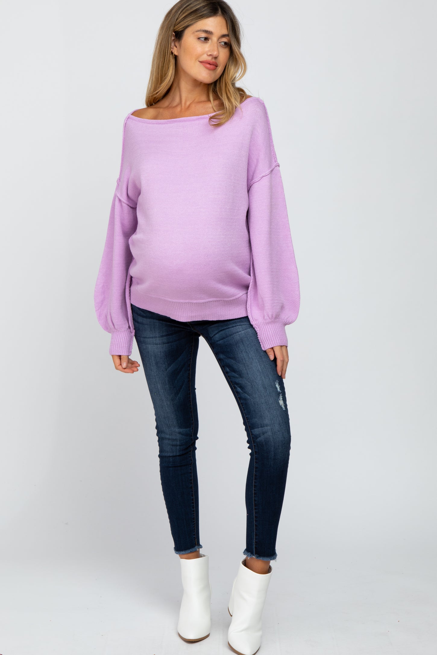woman wearing a light purple maternity sweater with balloon sleeves and a visible baby bump, paired with skinny jeans and ankle boots