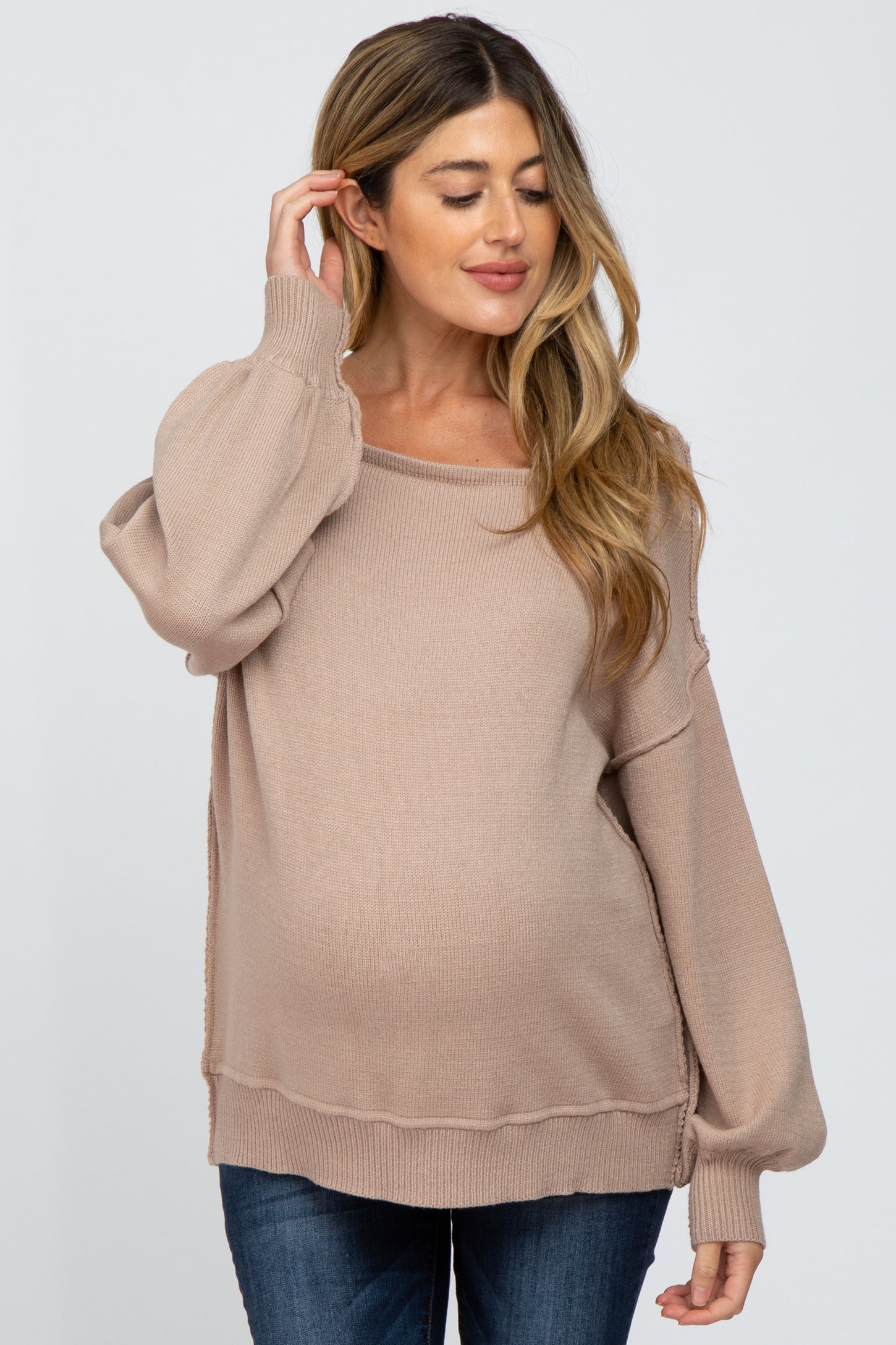 woman wearing a beige maternity sweater with a relaxed fit and balloon sleeves, showing her baby bump