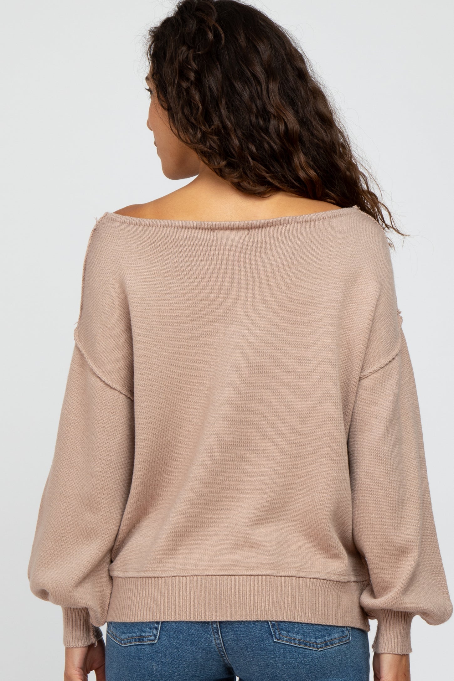 woman wearing a beige off-the-shoulder sweater with balloon sleeves, viewed from the back