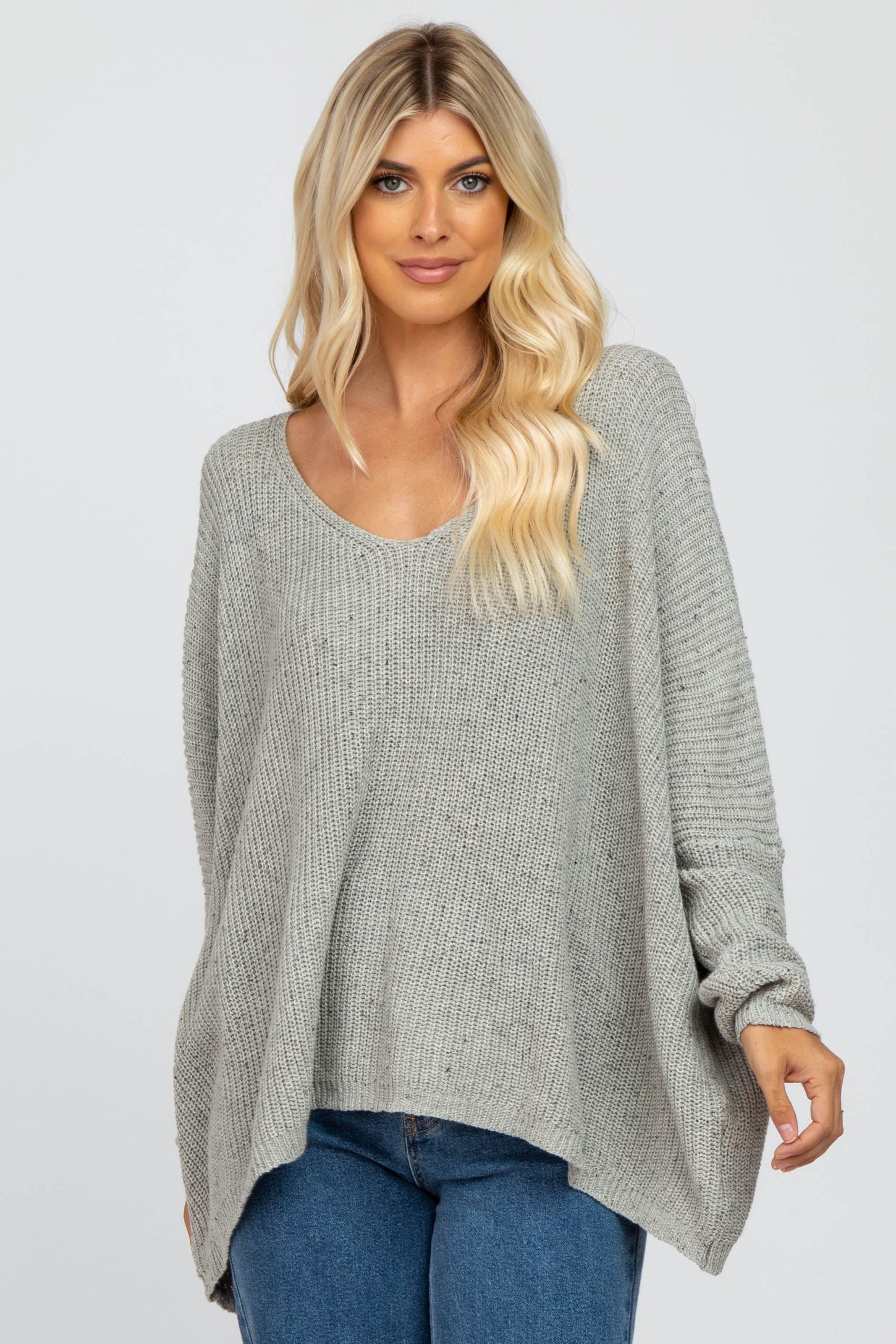 woman wearing a light gray oversized knit sweater with a scoop neckline and long sleeves, paired with blue jeans