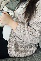 woman wearing a soft pink knitted maternity cardigan and black leggings, holding a mug, with a visible baby bump