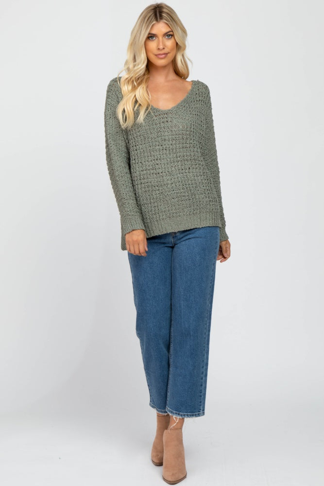 woman wearing an olive green crochet knit sweater and blue wide leg jeans with tan ankle boots