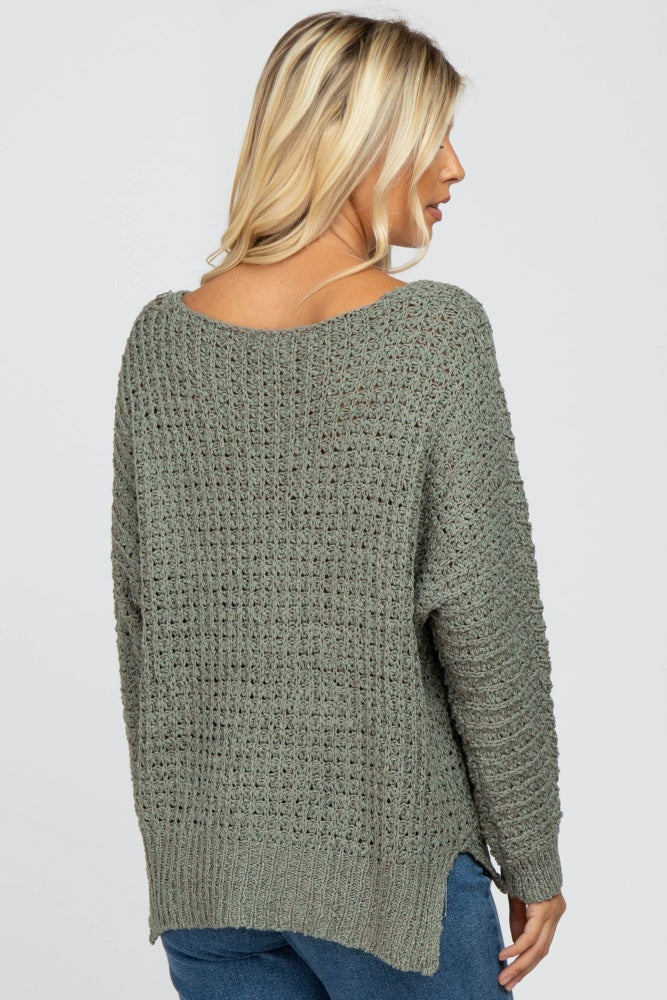 Back view of a woman wearing a sage green textured knit sweater with a scoop neckline and side slits.