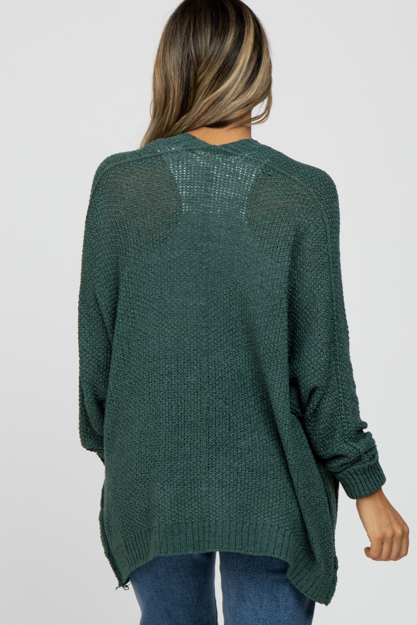 woman wearing a dark green oversized sweater with a textured knit design and side slits, seen from the back