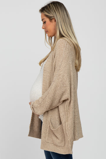 woman wearing a light beige open-knit maternity cardigan and holding her baby bump