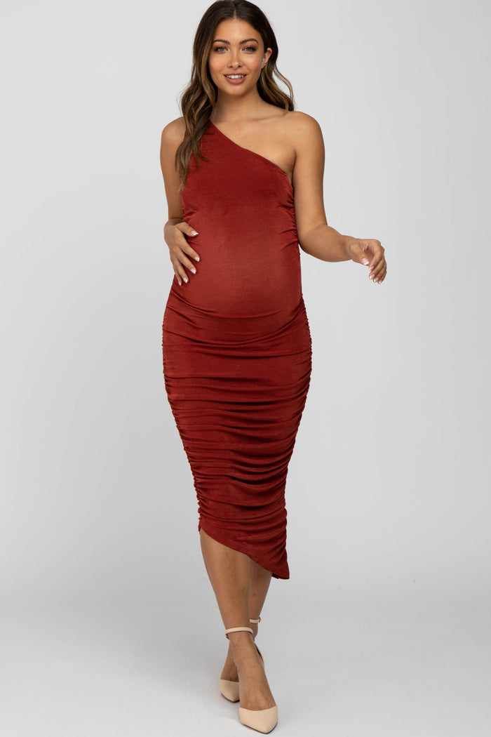 woman wearing a rust one-shoulder maternity dress with ruching and a visible baby bump
