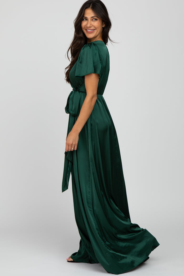 woman wearing a long green satin dress with short puff sleeves and a waist tie, facing sideways