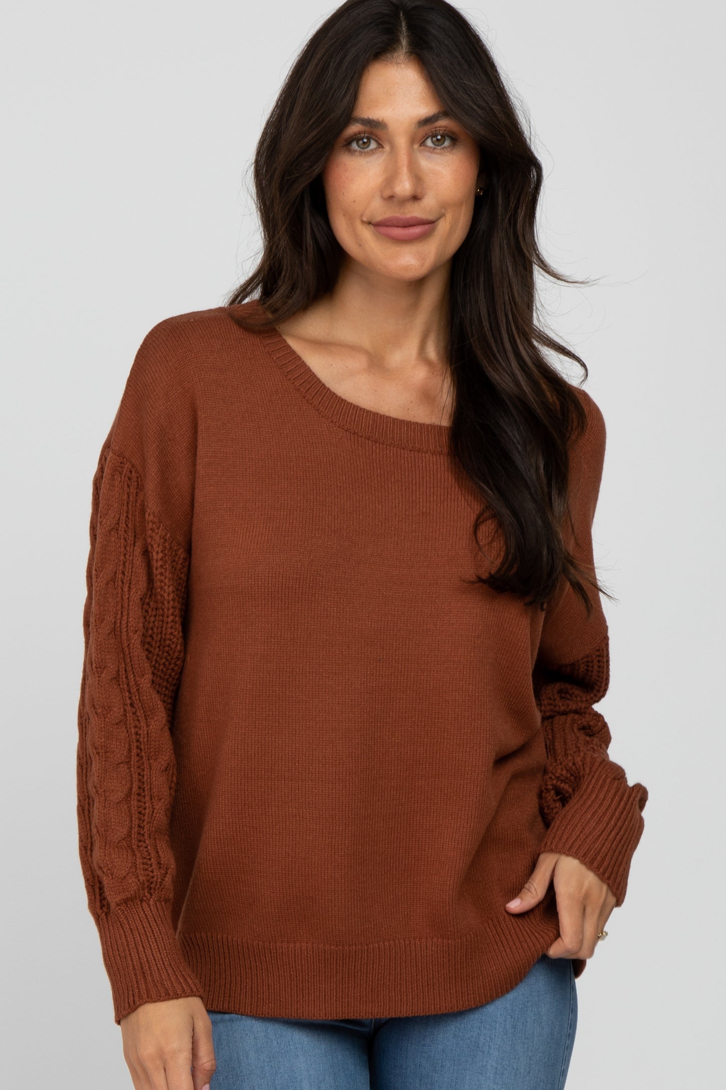 woman wearing a rust-colored oversized sweater with cable-knit sleeves and relaxed fit, paired with blue jeans