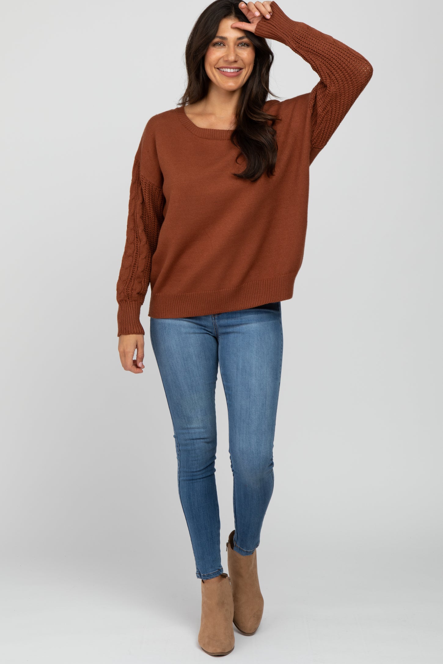 woman wearing a brown oversized sweater with cable knit sleeves paired with skinny jeans and ankle boots