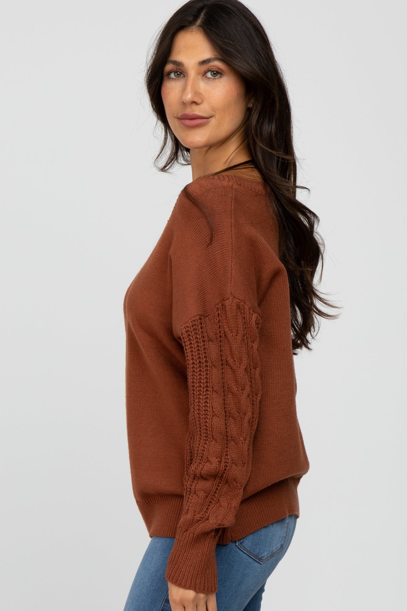 woman wearing a rust-colored sweater with cable knit sleeves and paired with denim jeans