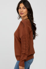 woman wearing a rust-colored sweater with cable knit sleeves and paired with denim jeans