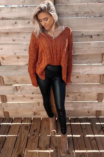 woman wearing an oversized orange cable knit sweater with black leather leggings and tan ankle boots