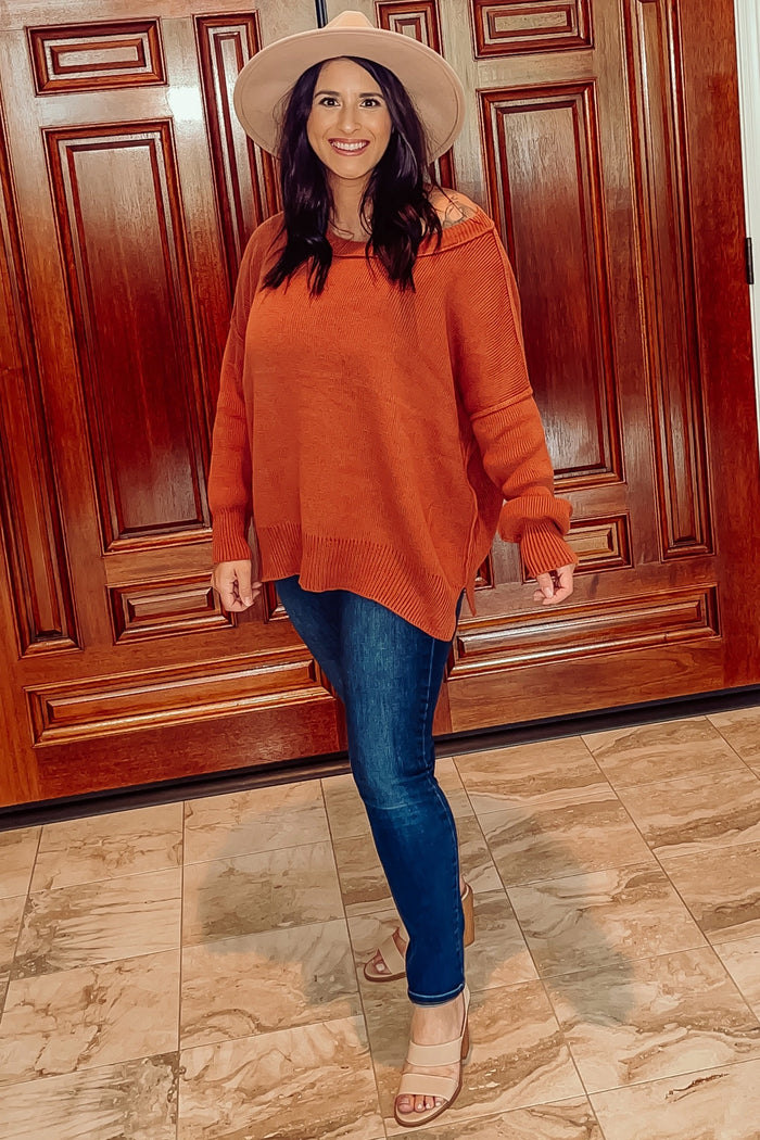 woman wearing an orange oversized sweater and blue skinny jeans, accessorized with a beige hat and nude heels