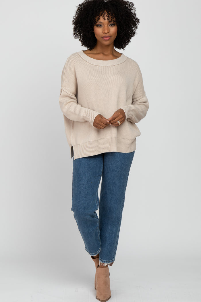 woman wearing a beige oversized knit sweater and blue high-waisted jeans, accessorized with beige ankle boots