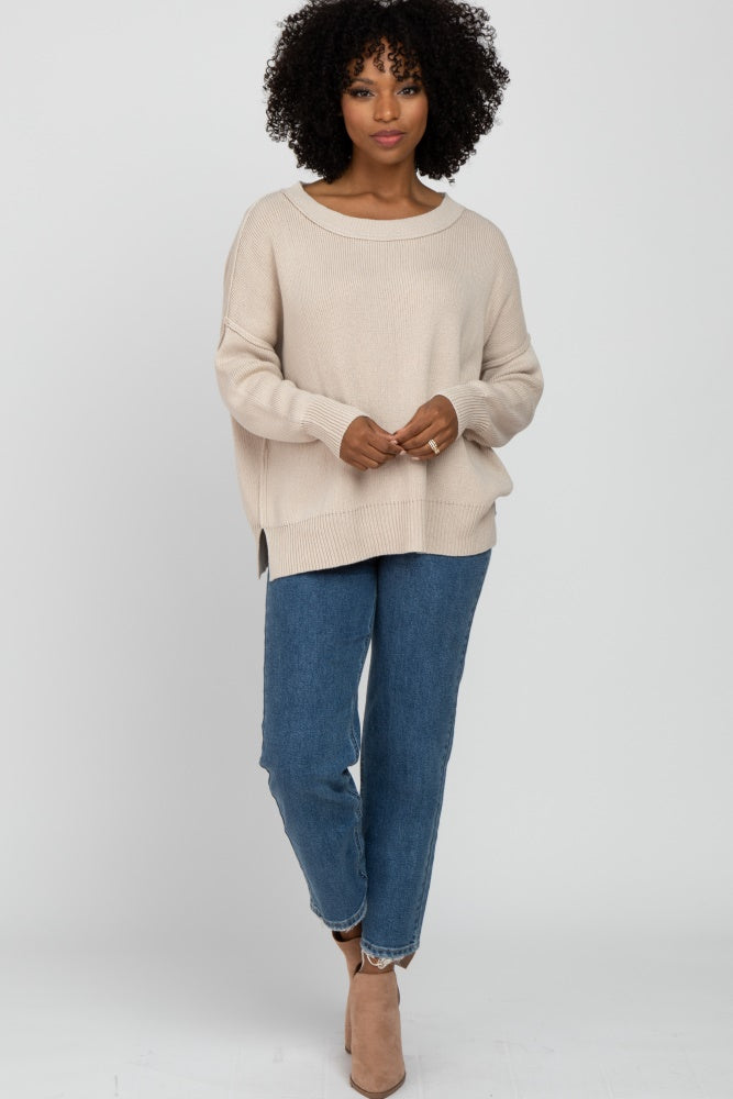 woman wearing a beige oversized knit sweater and blue high-waisted jeans, accessorized with beige ankle boots