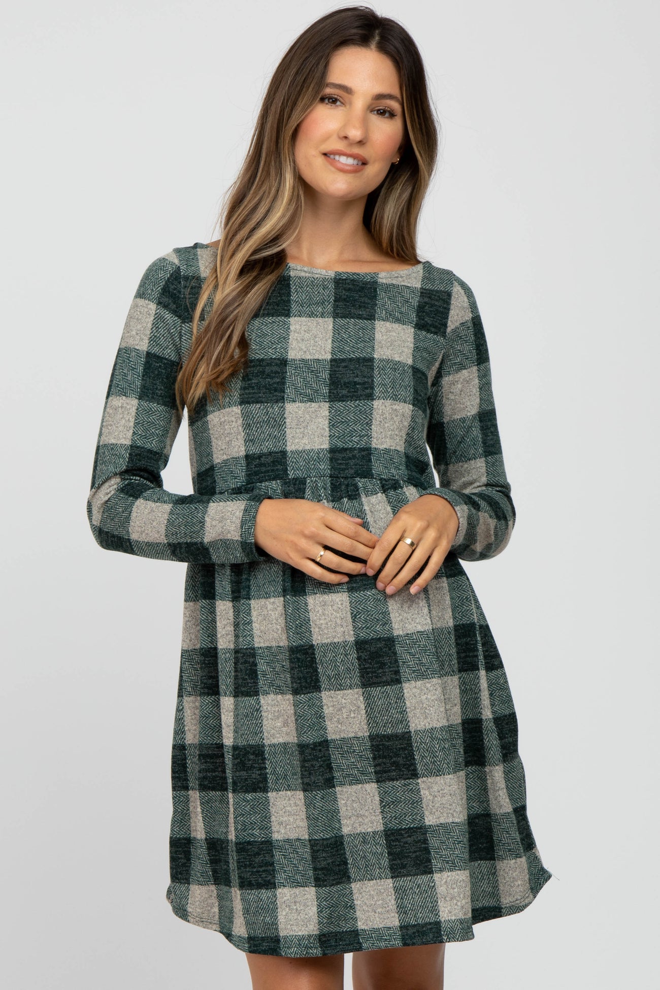 woman wearing a green and gray plaid maternity dress with long sleeves and a fitted waist, showing her baby bump