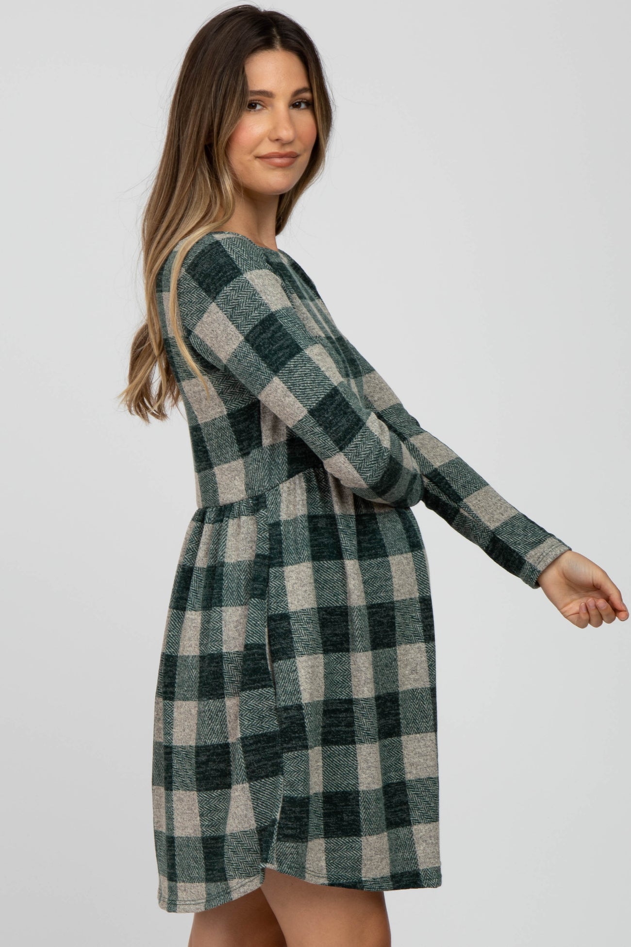 woman wearing a green and gray plaid long sleeve maternity dress and showing her baby bump