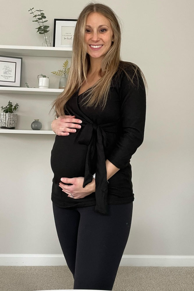 woman wearing a black maternity wrap top and black leggings, cradling her baby bump