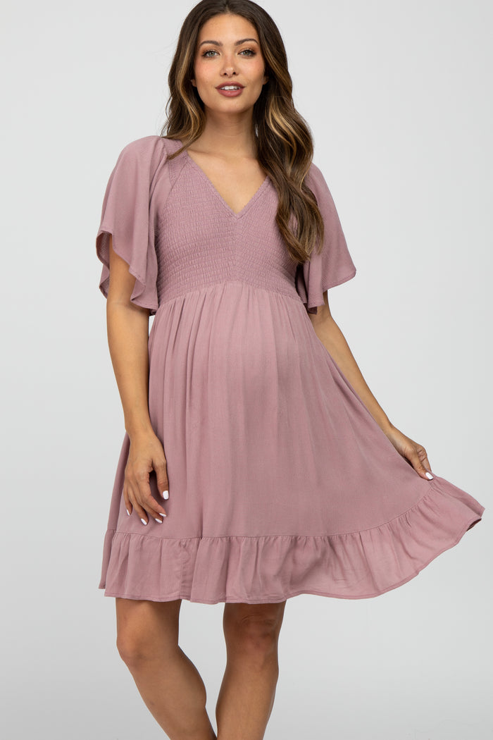woman wearing a mauve maternity dress with flutter sleeves, a smocked bodice, and a ruffled hem, highlighting her baby bump
