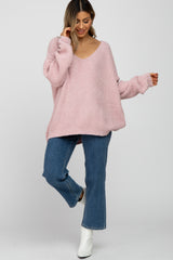 woman wearing a pink oversized v-neck sweater with long sleeves and blue flared jeans, posing with one foot raised