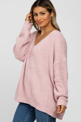 woman wearing a light pink oversized v-neck sweater with long sleeves and a relaxed fit paired with blue jeans
