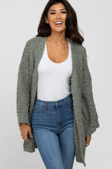 woman wearing a light olive green oversized textured cardigan over a white top and blue skinny jeans