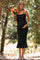 woman wearing a black maternity dress with ruffle details, holding a bouquet of flowers and gently cradling her baby bump