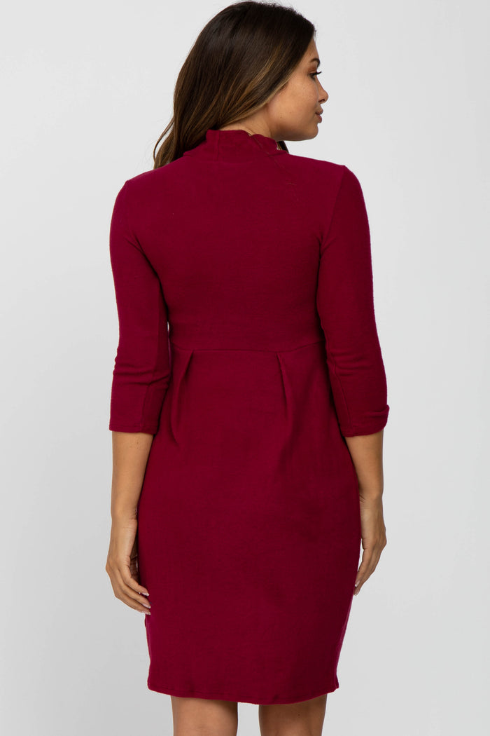 woman wearing a burgundy maternity dress with three-quarter sleeves and a pleated back design