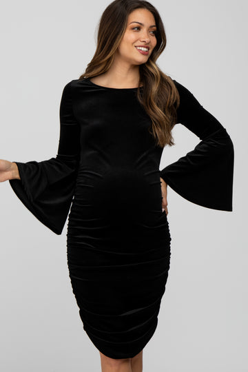 woman wearing a black velvet long sleeve maternity dress with bell sleeves and a visible baby bump